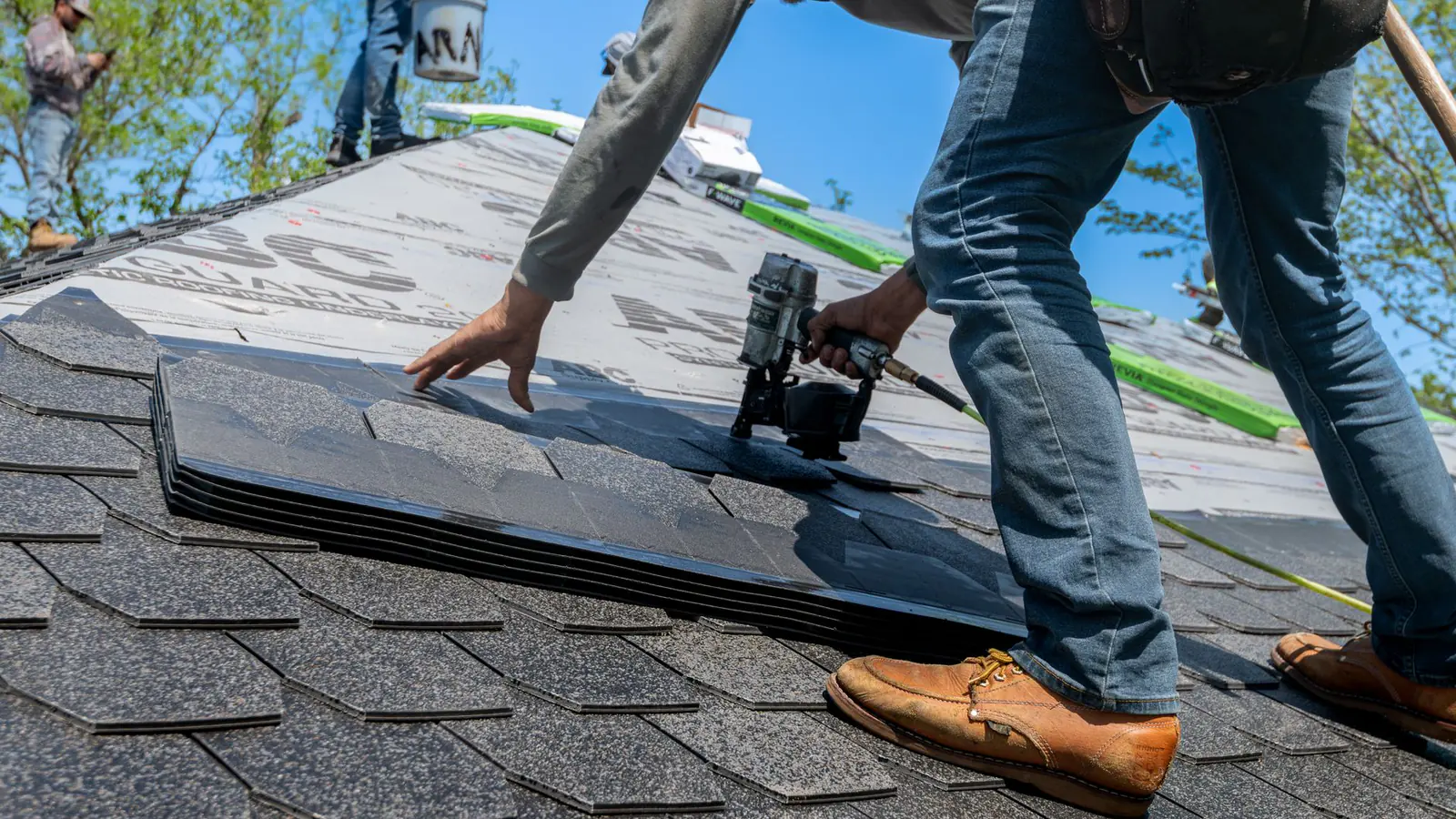 Roofer using nail gun for shingle installation on residential roof.