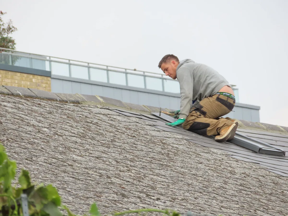 Construction worker installing asphalt shingles on a residential roof